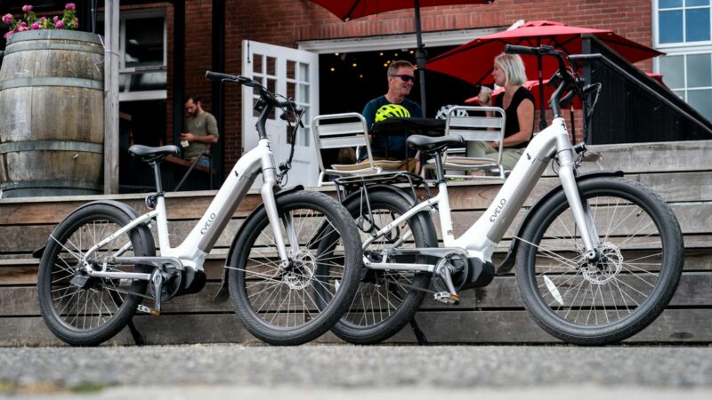 A Pair of White Electric Bikes Parked Near Couple Sitting Outside a Restaurant